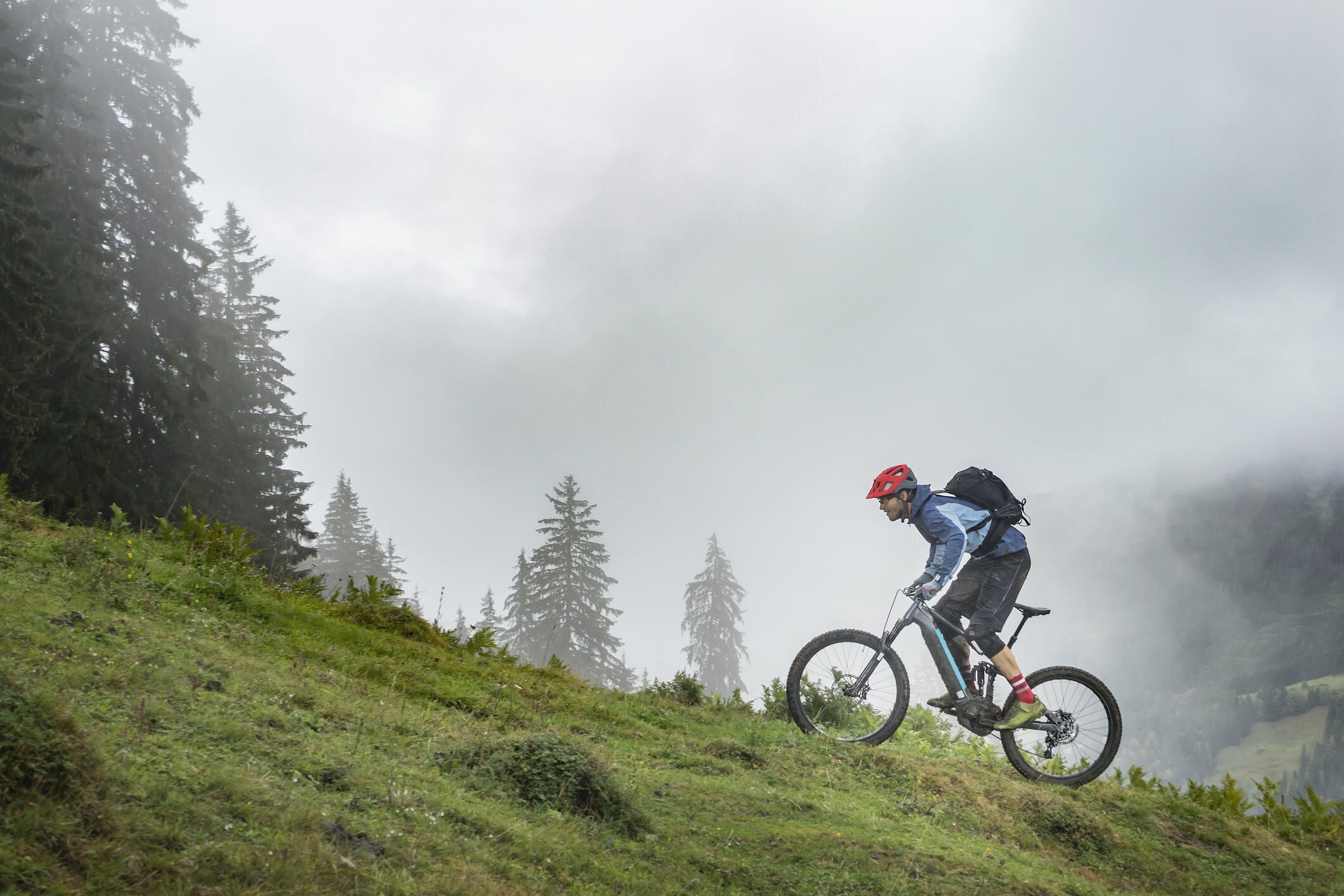 A man rides and e-bike up an incline on a mountain biking trail