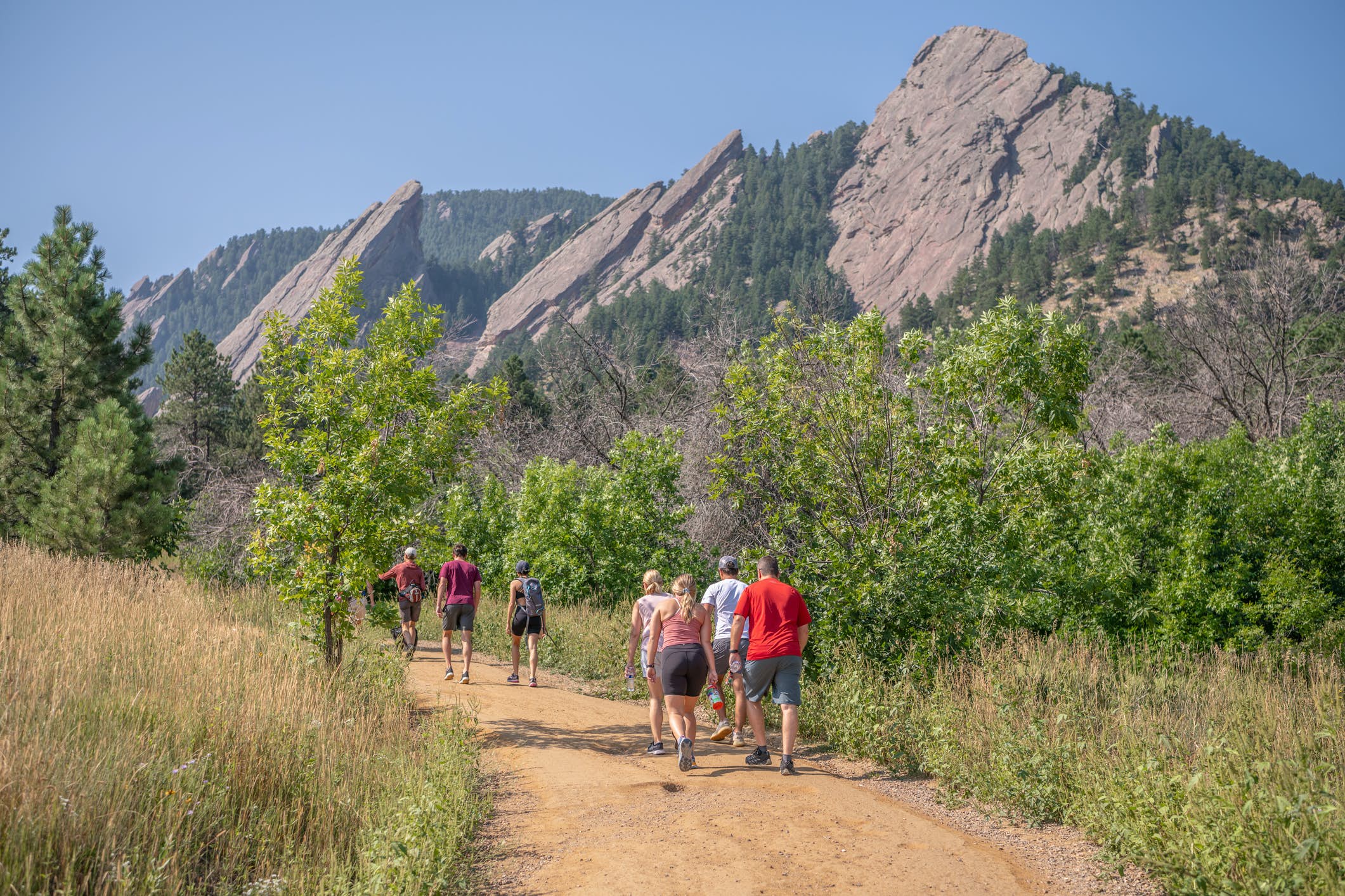 A group of hikers follow a trail on a sunny day heading towards huge, pointed, rocky outcrops