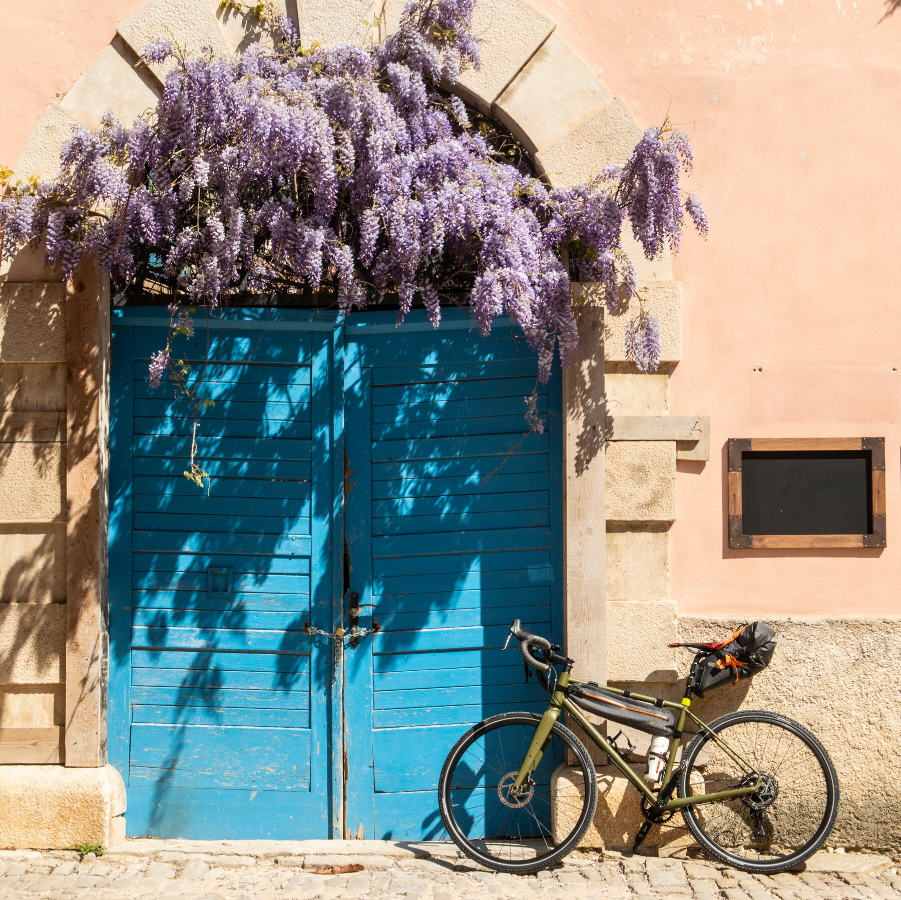 Bicycle on the outside wall of a building with a blue door.