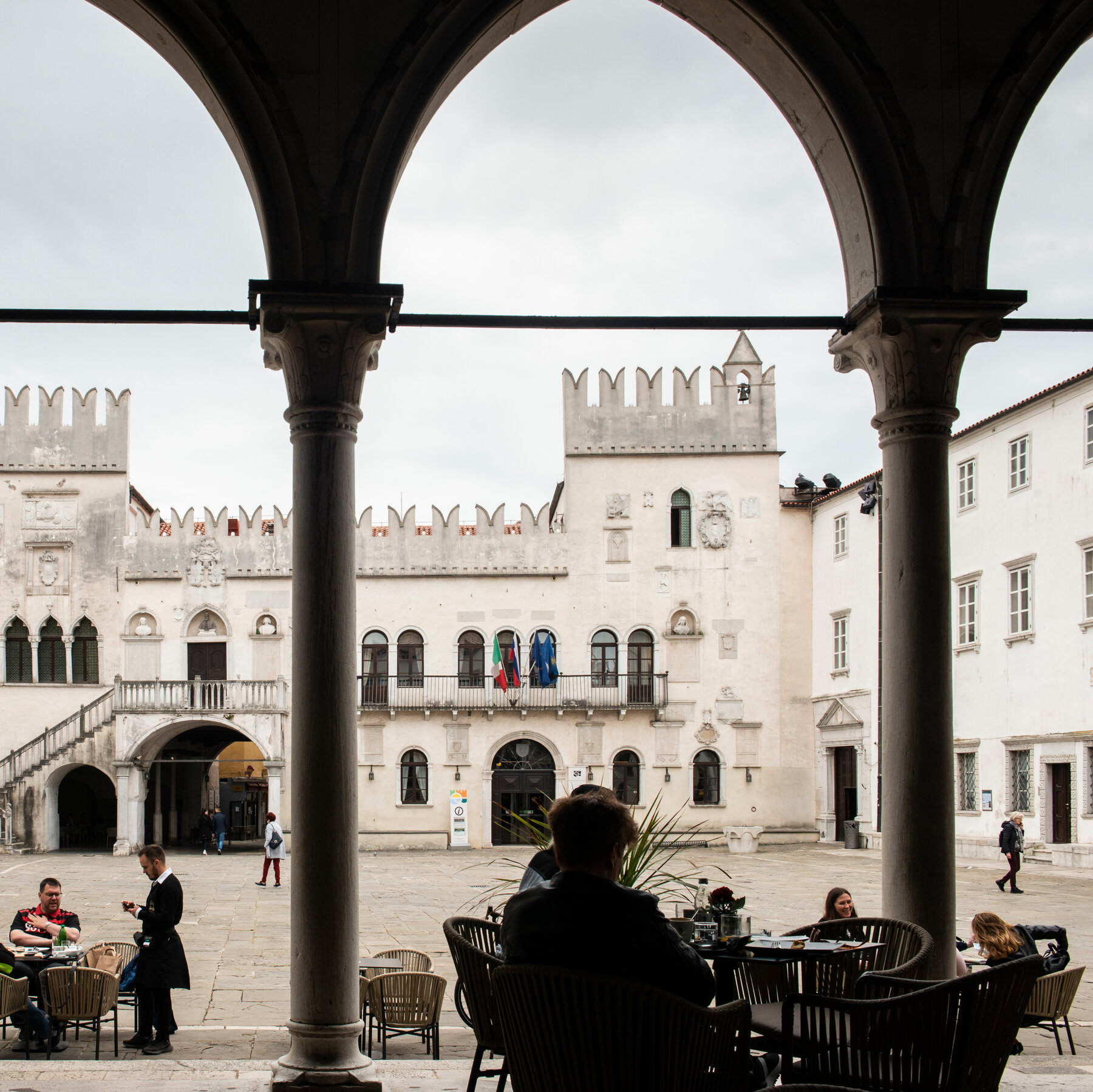 People sitting on tables at a restaurant near a square.