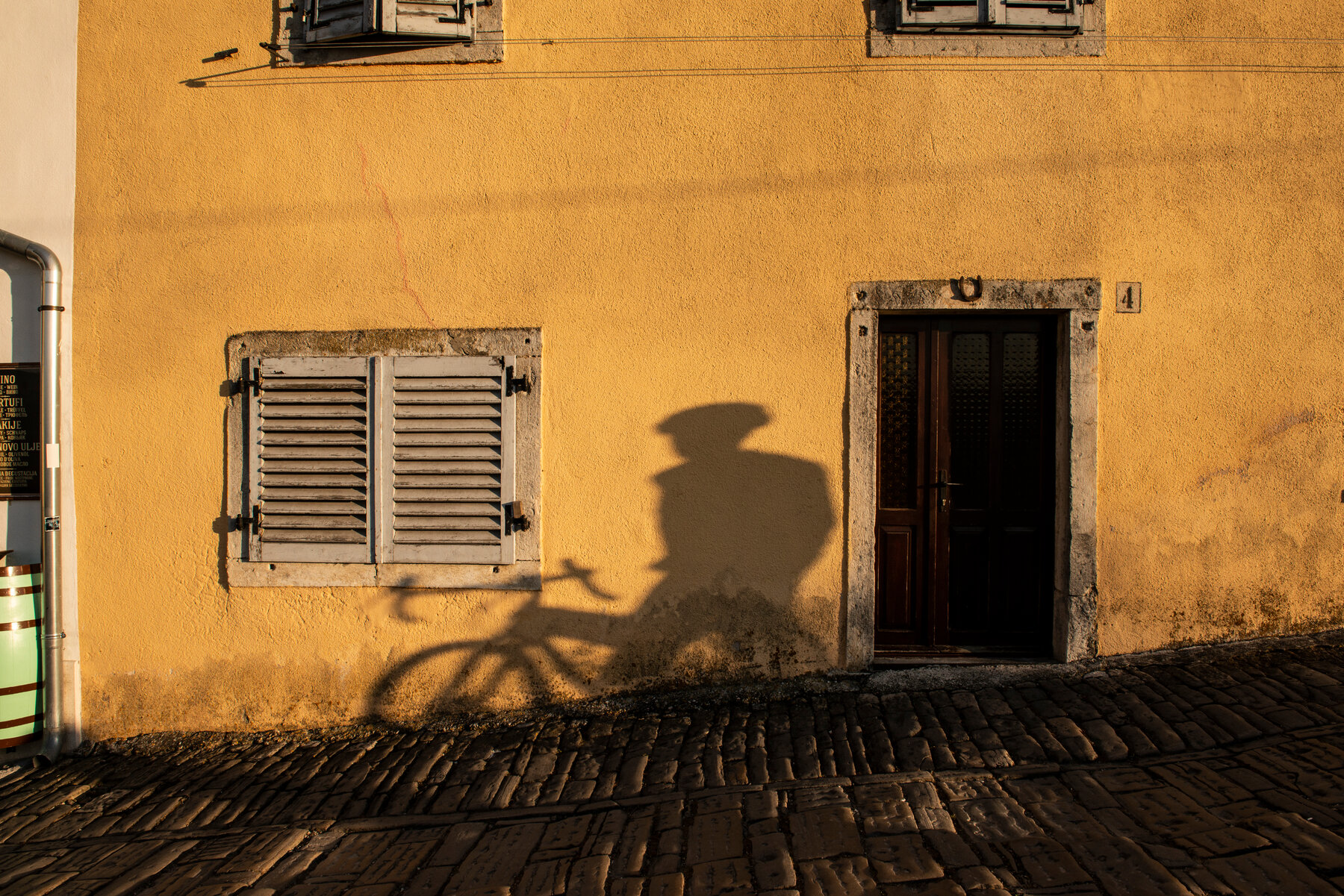 A shadow of a person and a bicycle over a wall.