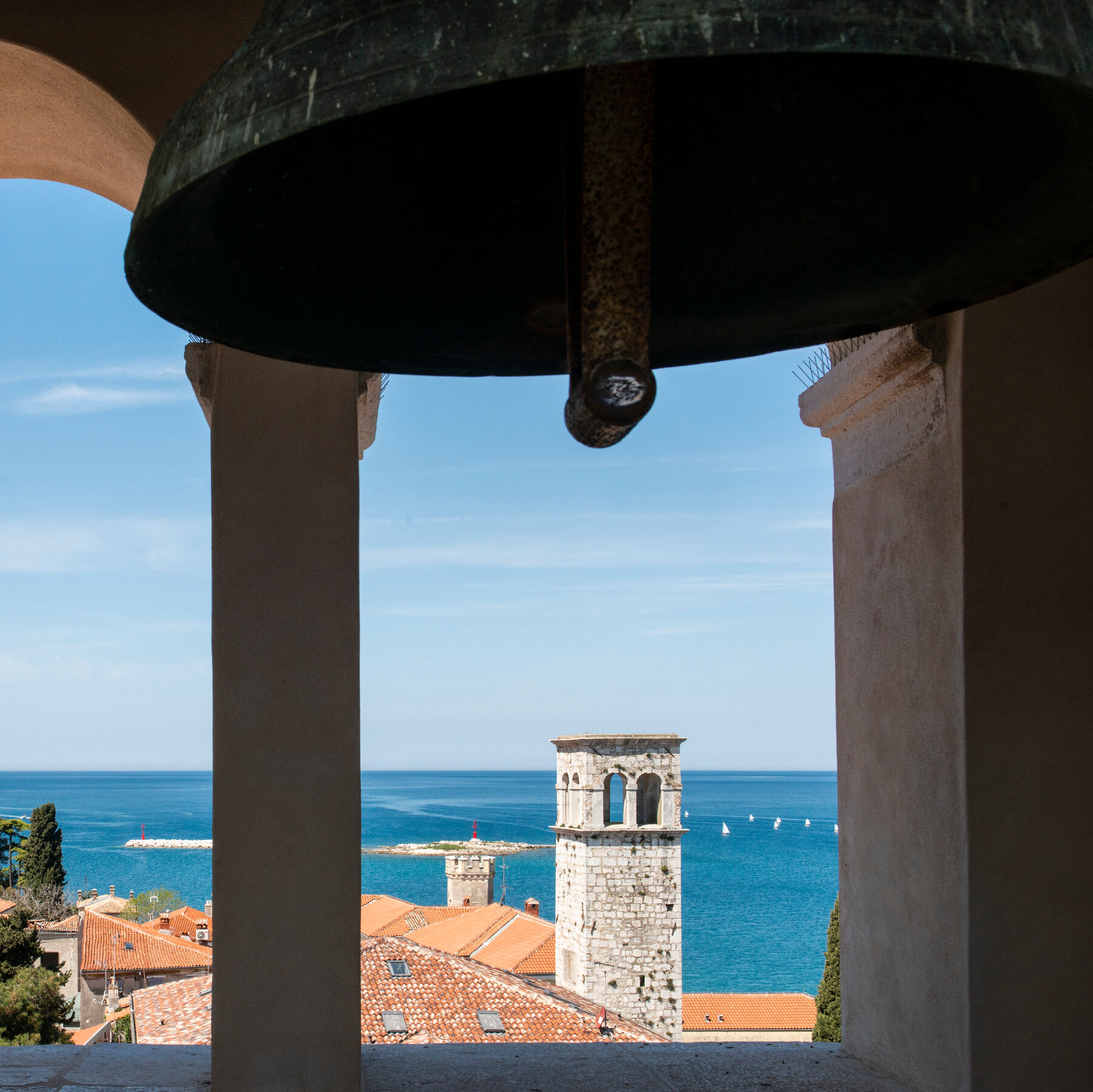 A view of roofs and a sea from a window in a room with large bells.