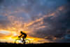A cyclist rides his road bike with the sun rising in the background.